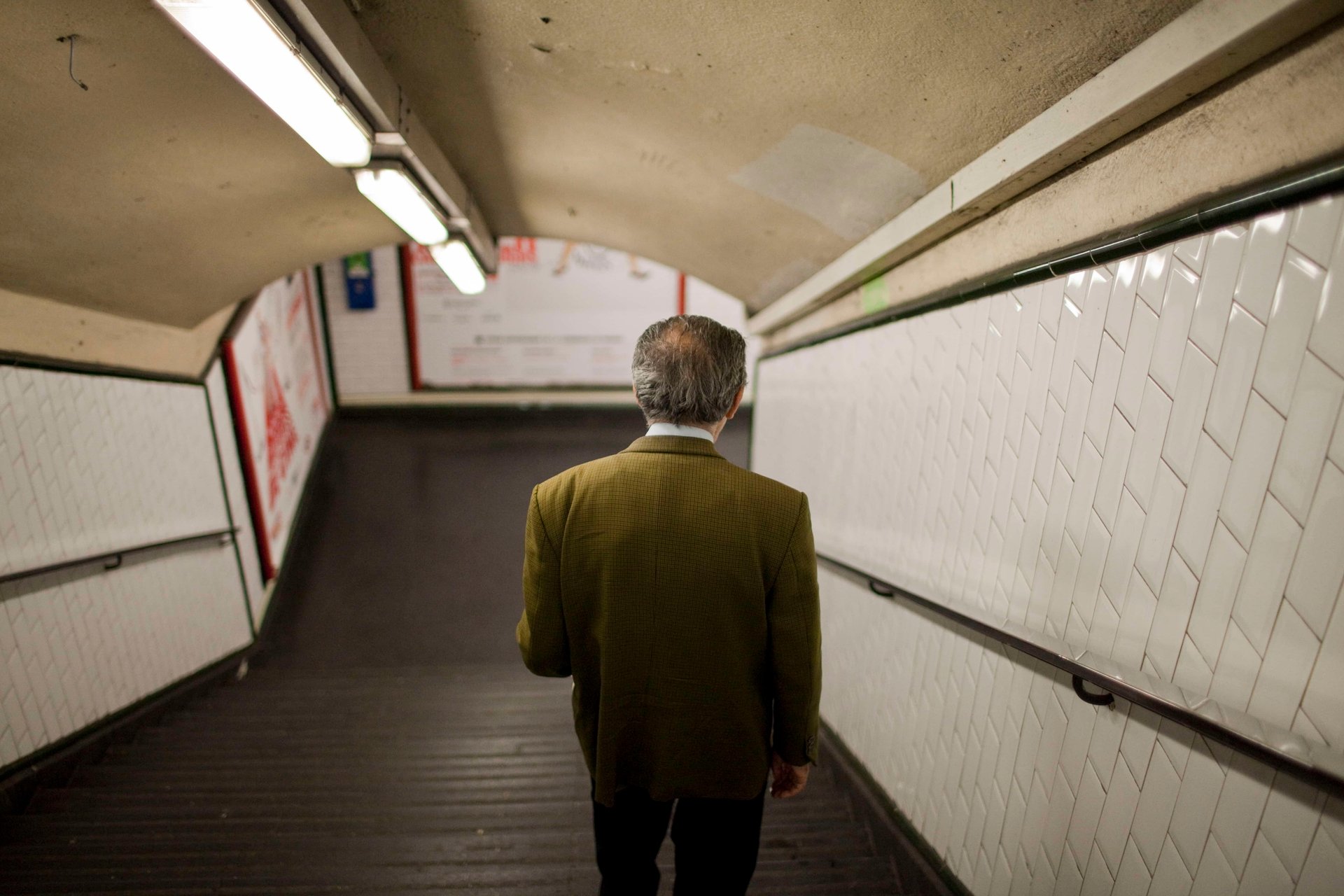 Homme âgé descendant les escaliers du métro parisien, veste verte
